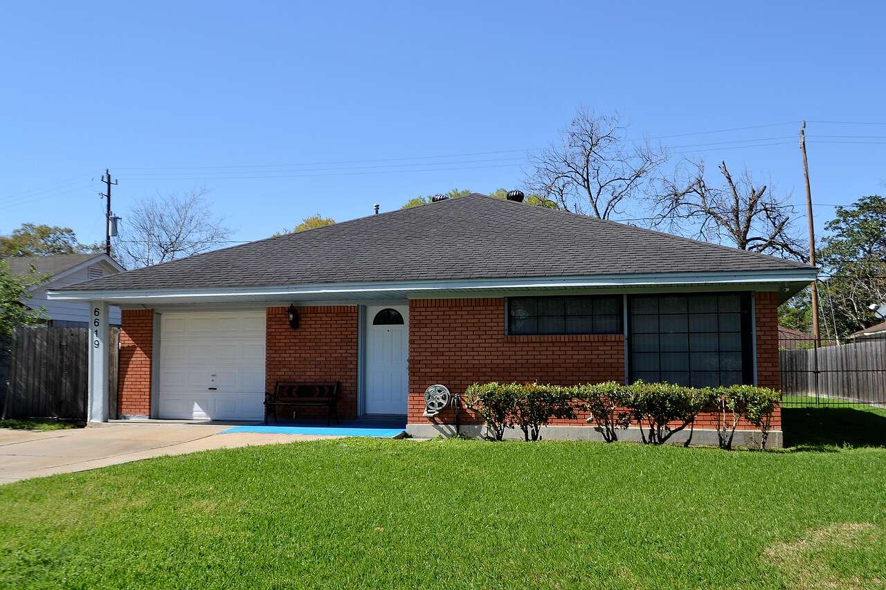 A single-story brick house with a composition shingle hip roof and a front lawn