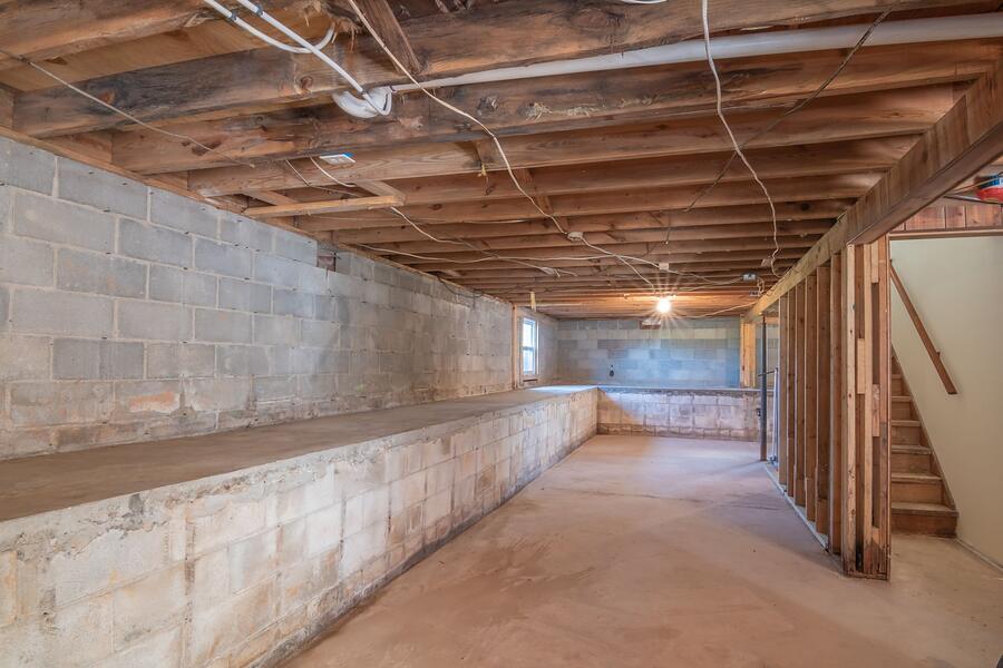 Exposed floor joists above a bare concrete floor beneath a house